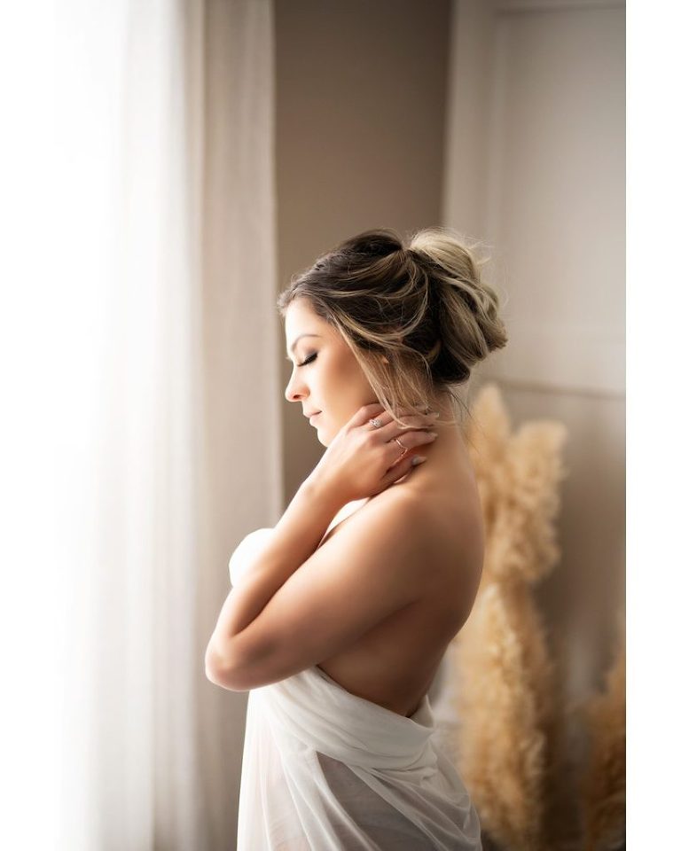 woman standing by window with hand by her neck wrapped in white sheet